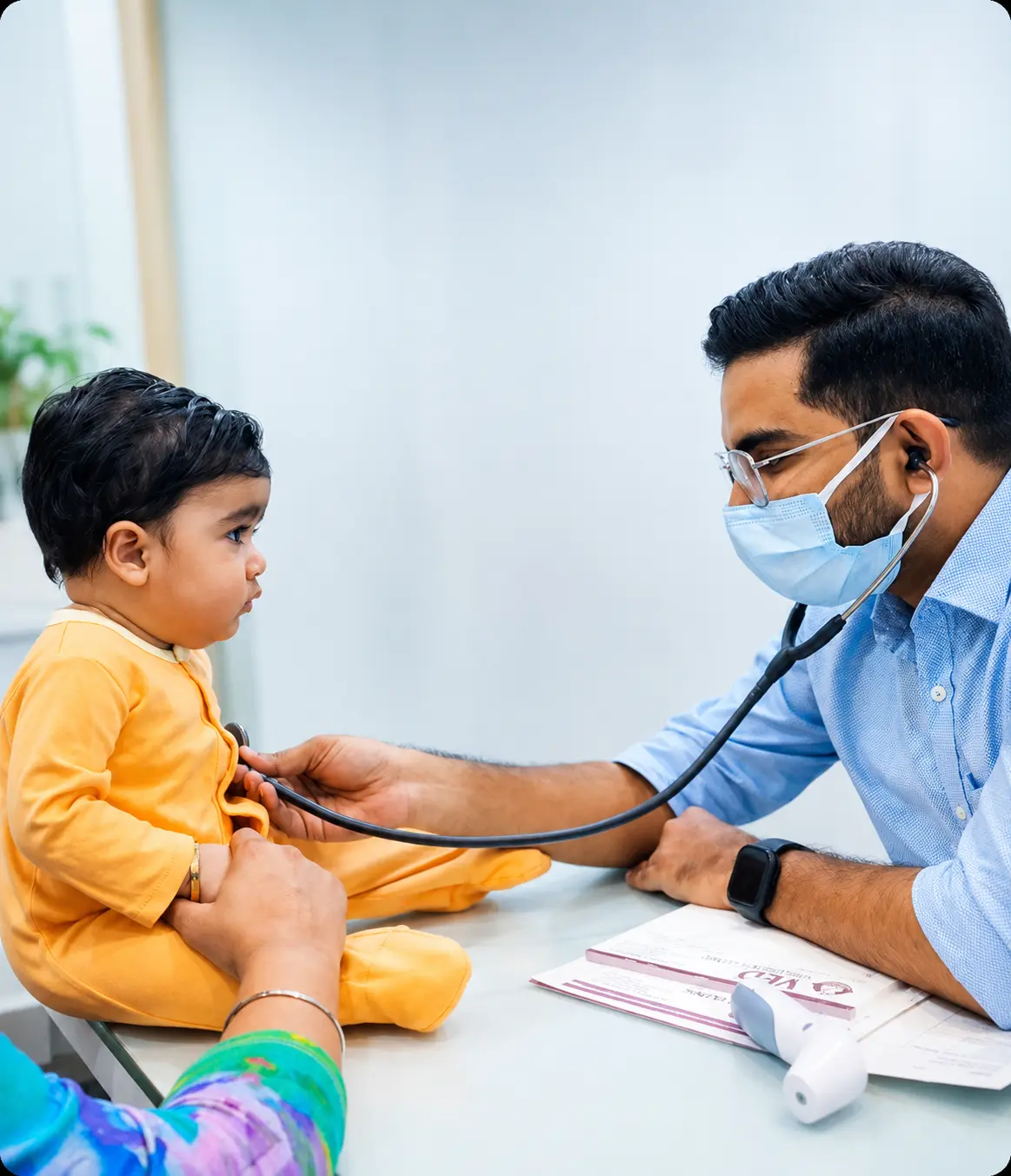 “Pediatric doctor examining a young child with a stethoscope in a clean clinic while a parent assists, showcasing professional child healthcare services.”